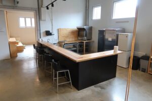 Moderne kantine met een houten bar, barkrukken en keukenapparatuur in een ruimte aan het Gedempt Hamerkanaal.